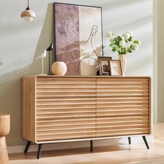 a wooden cabinet with an art piece on top of it next to a lamp and pictures