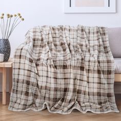 a plaid blanket sitting on top of a wooden table next to a vase with flowers