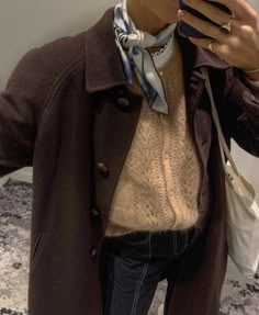 a woman taking a selfie with her cell phone while wearing a coat and scarf