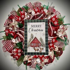 a christmas wreath with red and green decorations on it, featuring reindeers in front of a house