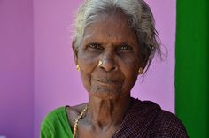 an old woman with white hair and piercings on her nose standing in front of a colorful wall