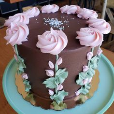 a chocolate cake with pink frosting and flowers on the top is sitting on a blue plate