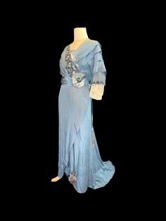 This exquisite antique original Edwardian evening dress, dating back to 1912, features a captivating blue satin fabric that embodies the elegance of its era. The bodice and sleeves are adorned with intricate blue floral patterns complemented by delicate black lace trim, enhancing its visual appeal. Both the front and back necklines showcase an insert of blue chiffon, elegantly finished with a beaded edge, while the neckline and the lower sections of the sleeves are crafted from fine white lace. Blue Satin Fabric, Beaded Edge, Velvet Accents, Black Lace Trim, Antique Blue, Edwardian Fashion, Blue Satin, Floral Patterns, Blue Velvet