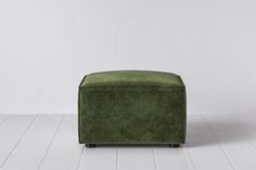 a green footstool sitting on top of a white floor next to a wall