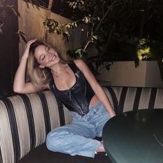 a beautiful woman sitting on top of a couch next to a green table and potted plant