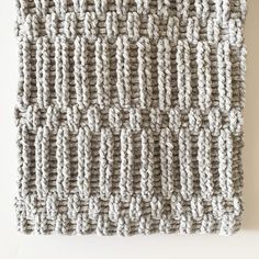 a knitted wall hanging on the side of a white wall