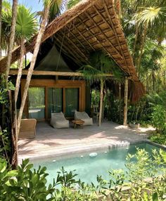 an outdoor area with a pool, lounge chairs and thatched roof over looking the jungle