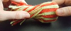 two hands are working on a piece of yarn that is red, yellow and green