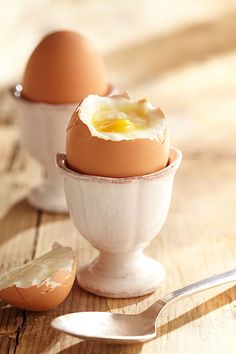 two eggs in an egg cup on a wooden table next to a fork and spoon