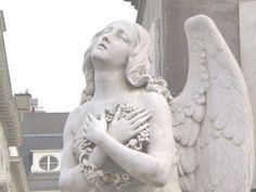 an angel statue holding a bouquet of flowers in front of a building on a city street