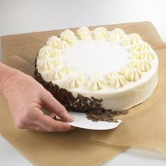 a person holding a knife over a cake on top of brown paper with white frosting