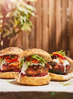 three burgers with meat, cheese and vegetables sitting on top of a wooden table