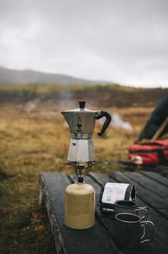 a coffee pot sitting on top of a wooden table next to a cup filled with liquid