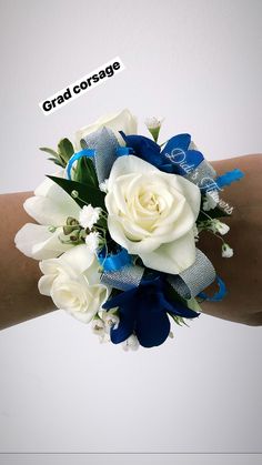 a wrist corsage with white roses and blue ribbons on it's arm