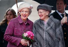 two older women standing under an umbrella in the rain, one holding a bouquet of flowers