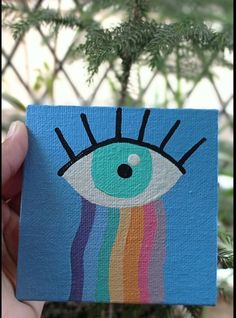 a hand holding up a small card with an eye painted on it