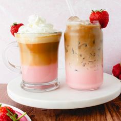 two drinks on a plate with strawberries and whipped cream in the glass next to each other