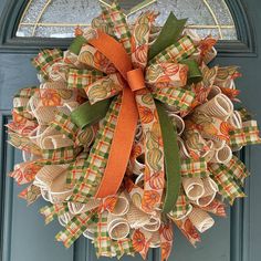 an orange and green wreath on the front door with ribbon hanging from it's side