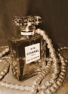 a chanel perfume bottle sitting on top of a table next to pearls and a necklace