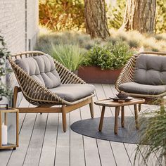 two wicker chairs sitting on top of a wooden deck next to potted plants