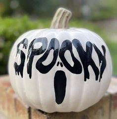 a white pumpkin with the word ghost painted on it's side sitting on top of a brick wall