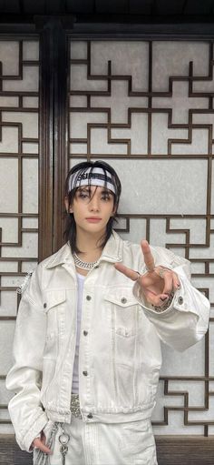 a woman in white is making the peace sign with her hand while standing next to a wall