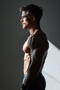 a man with no shirt standing in front of a white wall and looking off into the distance