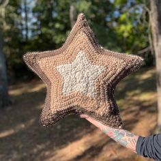 a person holding up a crocheted star ornament in front of trees