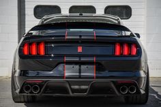 the rear end of a black sports car parked in front of a garage door with red stripes on it