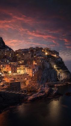 the city is lit up at night on top of a hill with water below it