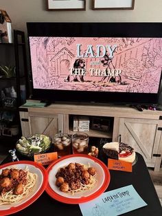 two plates of spaghetti and meatballs on a table in front of a flat screen tv