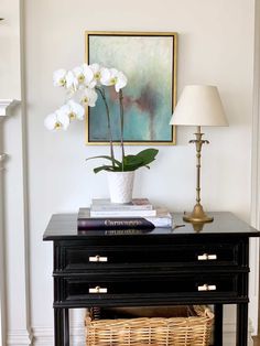 a black table with white flowers on top and a basket under the lamp next to it