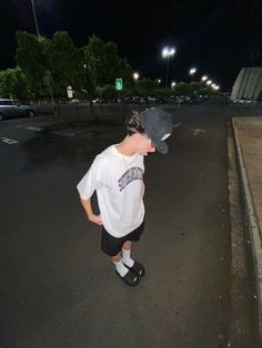 a young boy is standing in the middle of an empty parking lot at night with his hat on