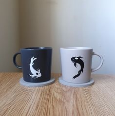 two coffee mugs with black and white designs on them sitting on a wooden table