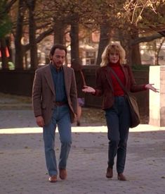 a man and woman walking down a sidewalk in front of some trees with their arms outstretched