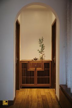 an archway leading into a room with a plant on top of the cabinet and wooden flooring