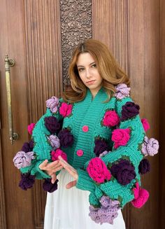 a woman standing in front of a wooden door wearing a green sweater with flowers on it