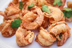 some shrimp is on a white plate and garnished with cilantro leaves