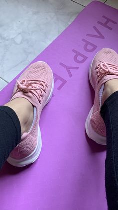 the feet of a woman who is sitting on a yoga mat with her pink shoes