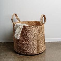 a large woven basket sitting on the floor next to a wall with a white rug