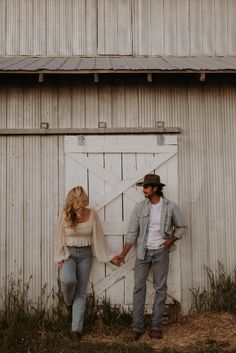 a man and woman holding hands standing in front of a barn door with the doors open