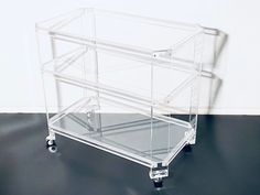 a clear plastic cart with wheels on the floor next to a white wall and black floor