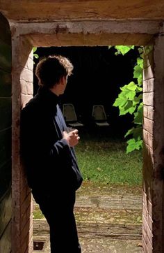 a man standing in an open doorway looking at his cell phone while wearing a black jacket