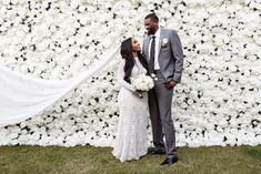 a bride and groom standing in front of a flower wall