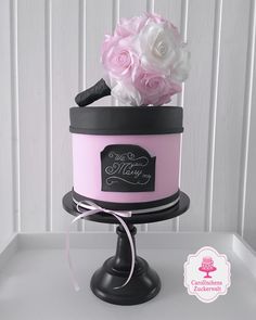 a pink and black cake with flowers on top is sitting on a stand in front of a white wall