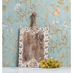 grapes are in front of an old photo frame on a table with floral wallpaper