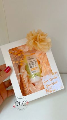 a hand holding an open box with some flowers in it and a bottle of lotion next to it