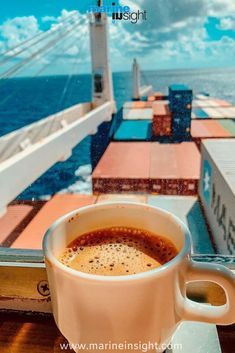 a cup of coffee sitting on top of a window sill next to the ocean