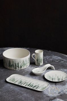 three white dishes and two spoons with trees on them sitting on top of a table