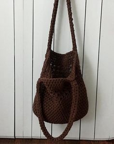 a crocheted purse hanging from a hook on a white wooden wall next to a door